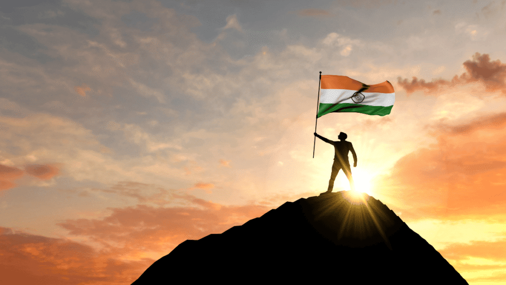Person standing on mountain peak holding India’s national flag at sunrise, celebrating Independence Day.
